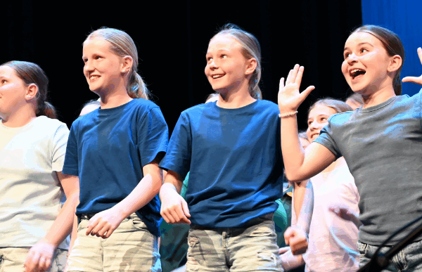 Kids performing on stage in navy, white and grey shirts