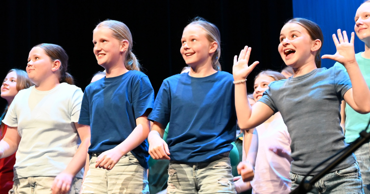 Kids performing on stage in navy, white and grey shirts