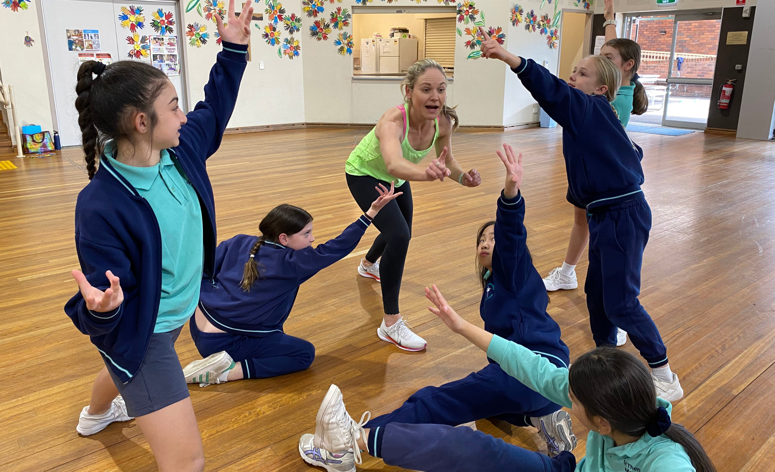 dance instructor teaching children in navy and green primary school uniform